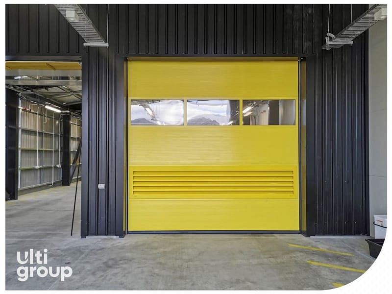 Yellow sectional industrial door with vision panels and ventilation slats.